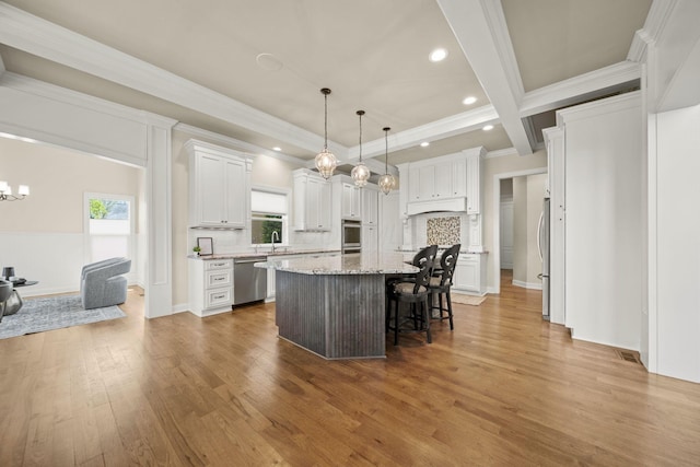kitchen featuring crown molding, wood finished floors, a kitchen island, a breakfast bar area, and appliances with stainless steel finishes