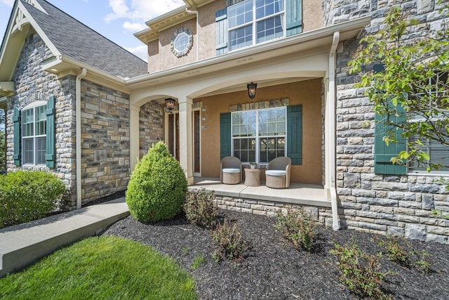 view of exterior entry with roof with shingles, a porch, and stone siding