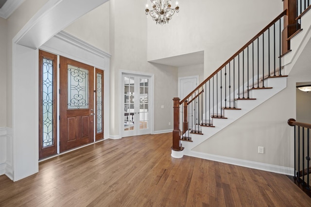 foyer entrance with baseboards, a high ceiling, an inviting chandelier, and wood finished floors