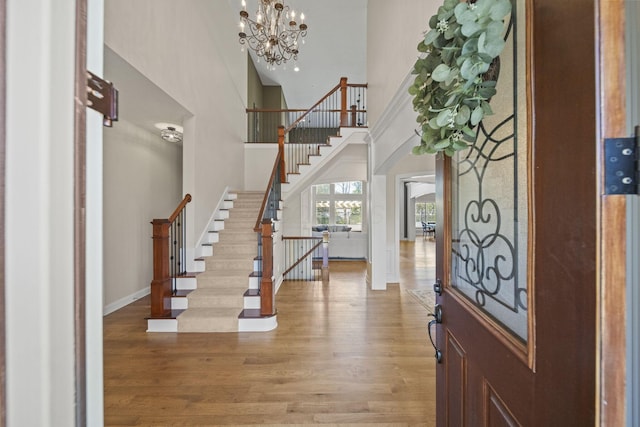 entrance foyer featuring wood finished floors, baseboards, an inviting chandelier, a high ceiling, and stairs