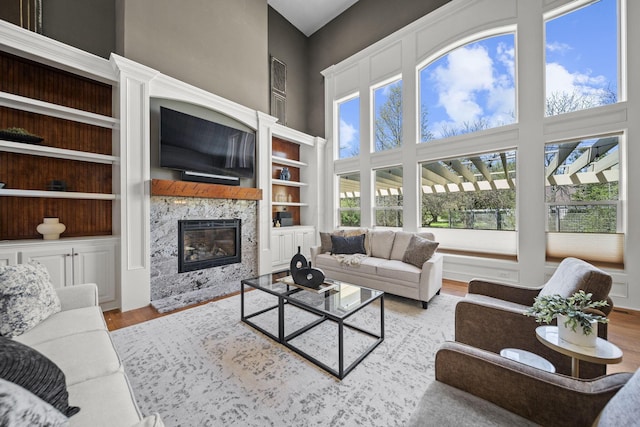living area featuring a premium fireplace, a high ceiling, built in shelves, and wood finished floors