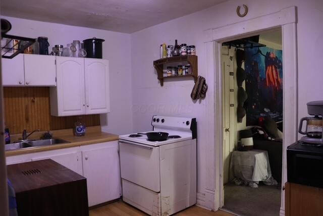 kitchen with white electric range oven, light wood-type flooring, light countertops, white cabinets, and a sink