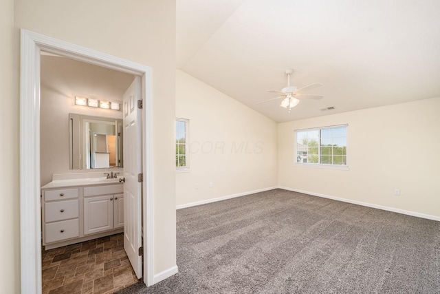 unfurnished bedroom featuring connected bathroom, a sink, dark colored carpet, baseboards, and vaulted ceiling