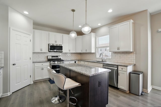 kitchen with a kitchen island, appliances with stainless steel finishes, a sink, baseboards, and white cabinets