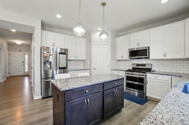 kitchen featuring white cabinets, appliances with stainless steel finishes, wood finished floors, a kitchen island, and pendant lighting
