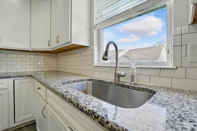 kitchen featuring a sink, backsplash, white cabinets, and light stone countertops