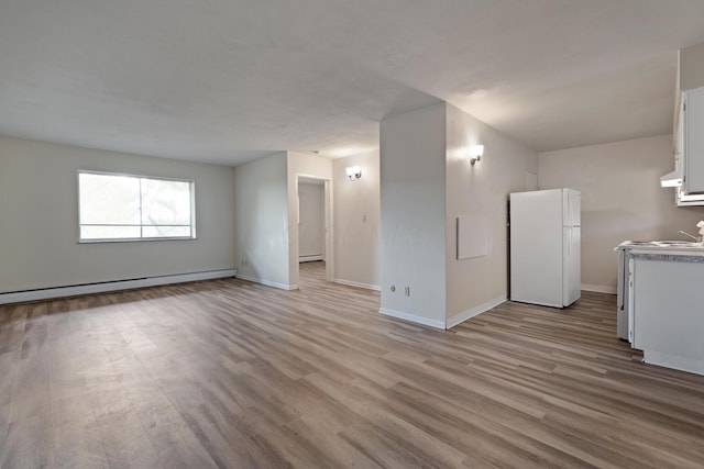 unfurnished living room with a baseboard heating unit, wood finished floors, and baseboards