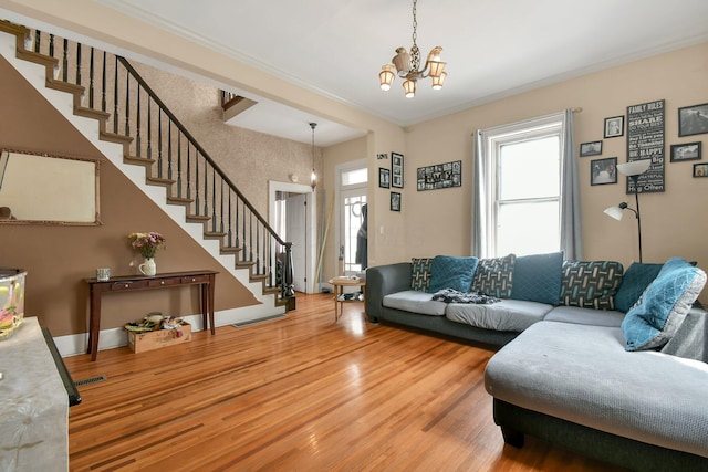 living area featuring stairs, ornamental molding, light wood-type flooring, visible vents, and a notable chandelier