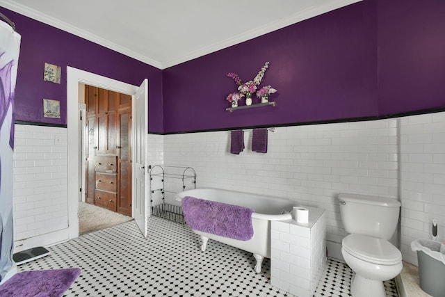 bathroom with a tub, tile walls, a wainscoted wall, toilet, and crown molding