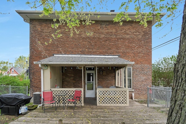 rear view of property with cooling unit, brick siding, a deck, and fence