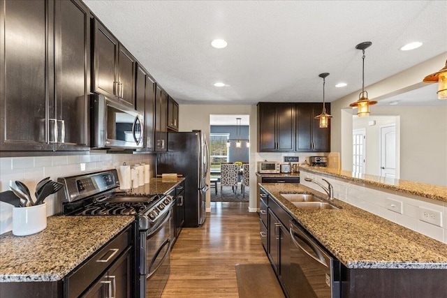 kitchen with dark brown cabinets, a sink, stainless steel appliances, decorative backsplash, and wood finished floors