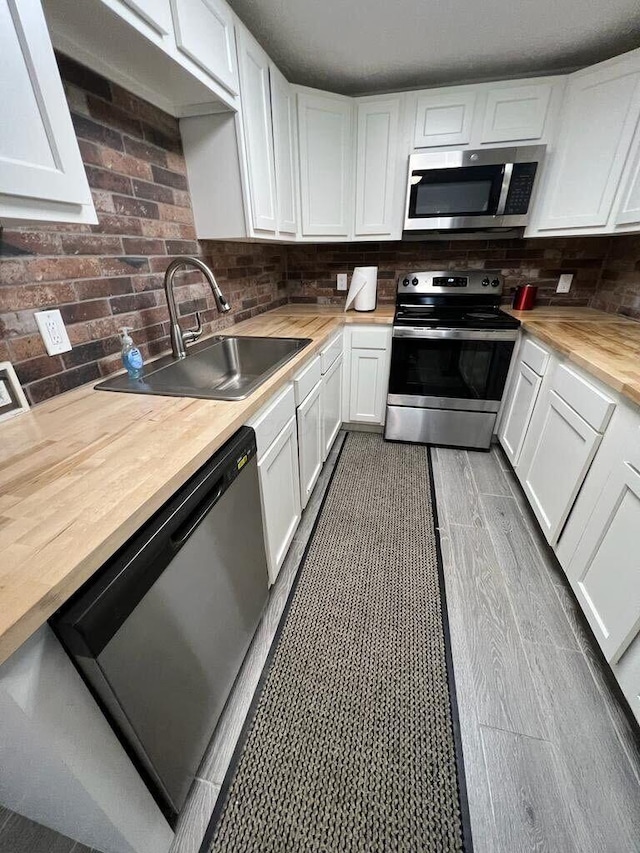 kitchen with white cabinets, wood counters, appliances with stainless steel finishes, and a sink