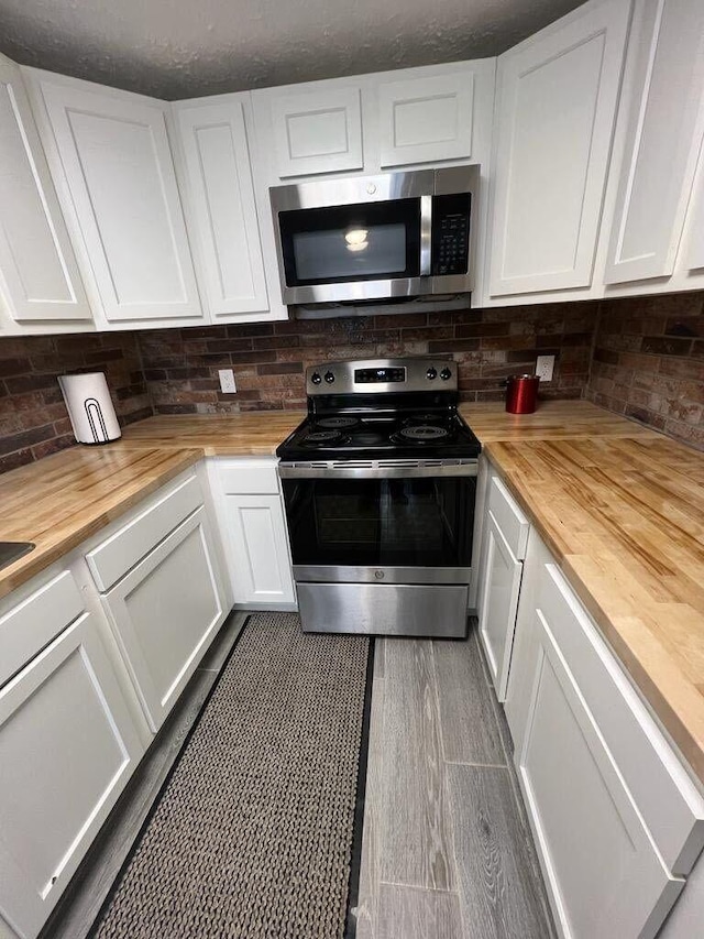 kitchen with appliances with stainless steel finishes, white cabinets, decorative backsplash, and butcher block counters