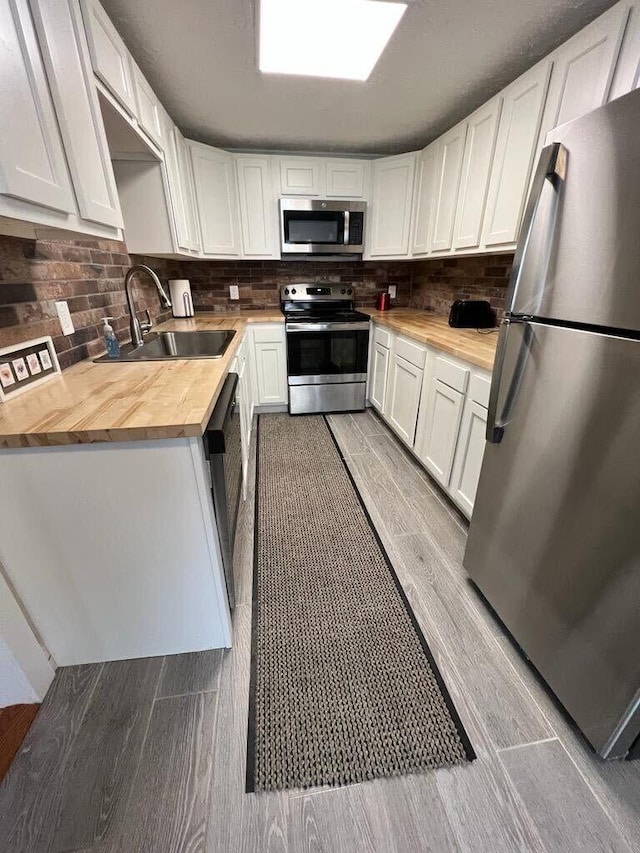 kitchen featuring a sink, stainless steel appliances, butcher block countertops, and white cabinetry