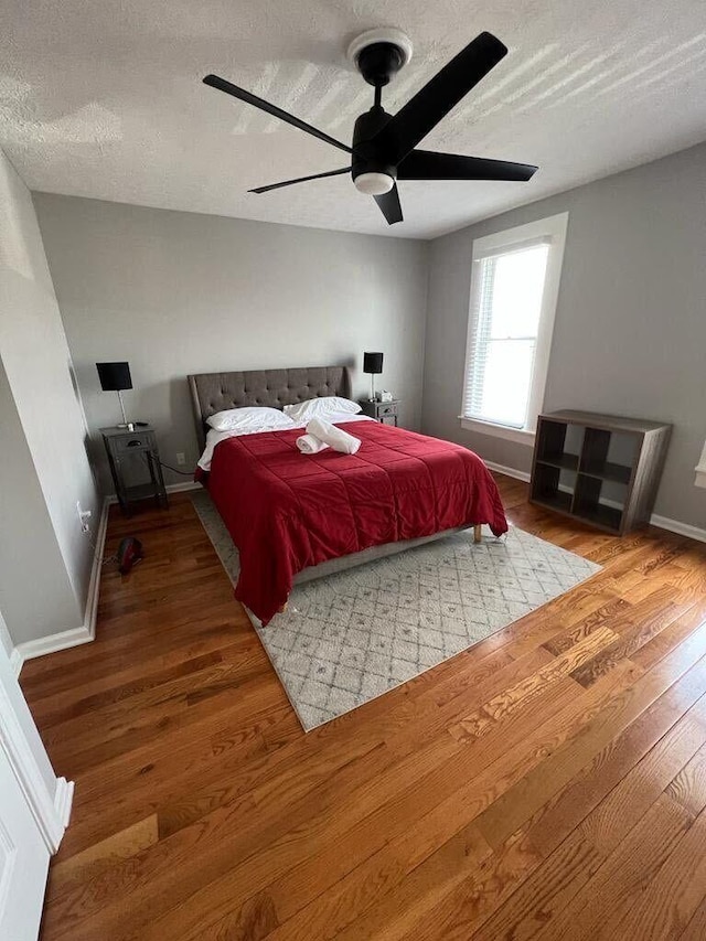 bedroom featuring baseboards, a textured ceiling, ceiling fan, and wood finished floors