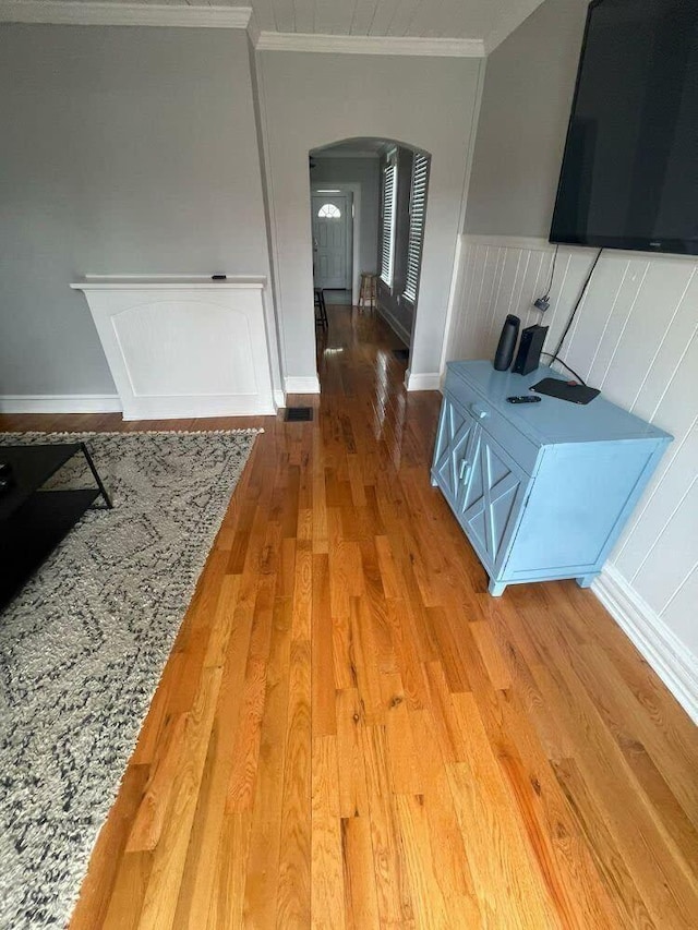 corridor featuring crown molding, arched walkways, wainscoting, and wood finished floors