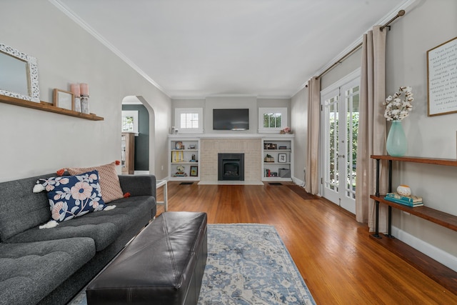 living area featuring arched walkways, baseboards, ornamental molding, and wood finished floors