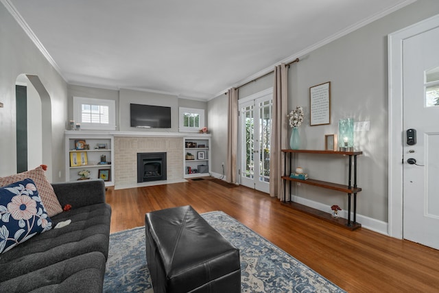 living area featuring crown molding, a brick fireplace, wood finished floors, baseboards, and arched walkways