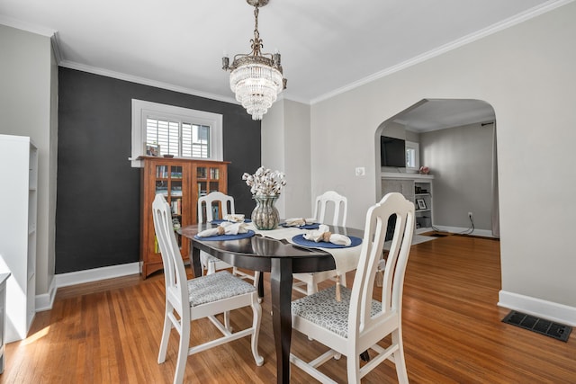 dining area featuring arched walkways, a chandelier, baseboards, wood finished floors, and visible vents
