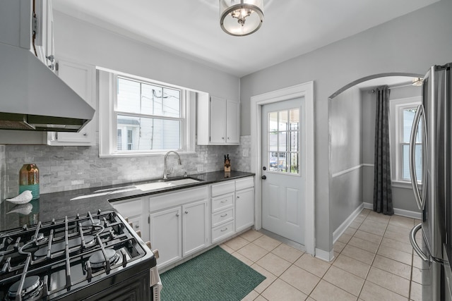kitchen featuring decorative backsplash, freestanding refrigerator, dark countertops, gas range, and a sink