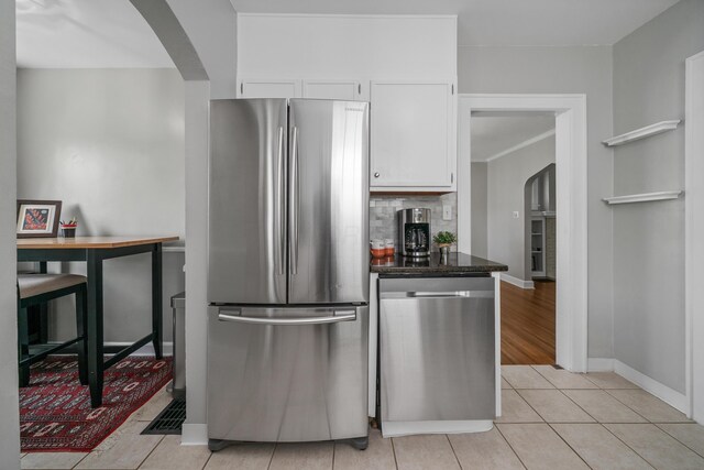 kitchen featuring light tile patterned flooring, appliances with stainless steel finishes, arched walkways, white cabinetry, and baseboards