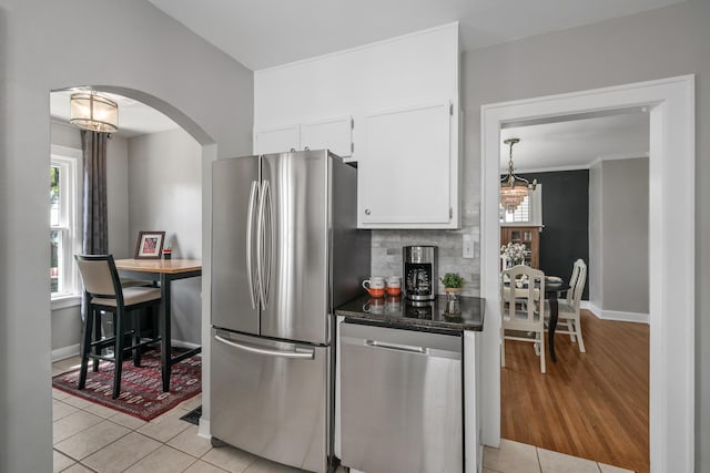 kitchen featuring arched walkways, white cabinets, an inviting chandelier, stainless steel appliances, and light tile patterned flooring