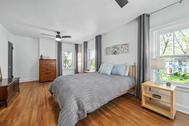 bedroom featuring baseboards, multiple windows, a ceiling fan, and wood finished floors