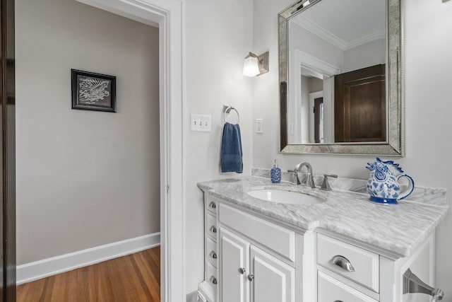 bathroom featuring baseboards, ornamental molding, wood finished floors, and vanity