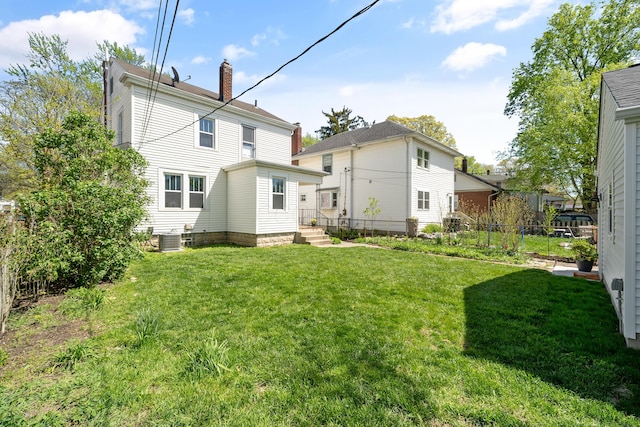 back of property with fence, central AC unit, a chimney, and a yard