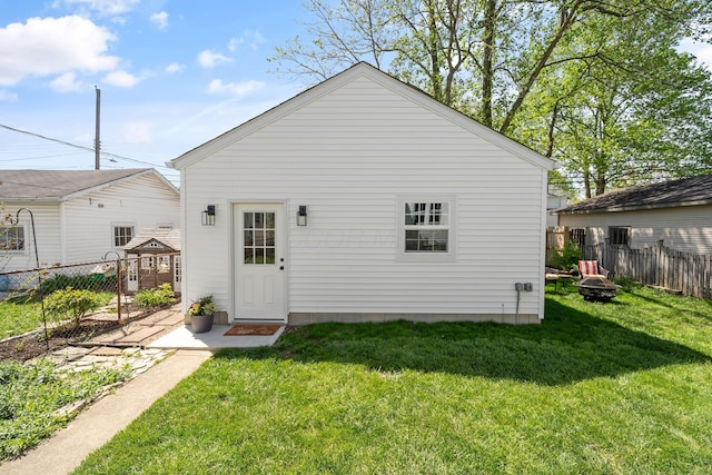 rear view of house featuring an outdoor fire pit, fence, and a yard