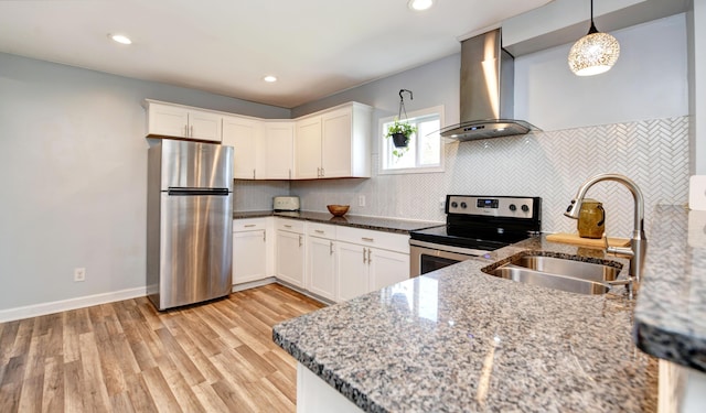 kitchen with light stone counters, a sink, appliances with stainless steel finishes, and wall chimney range hood