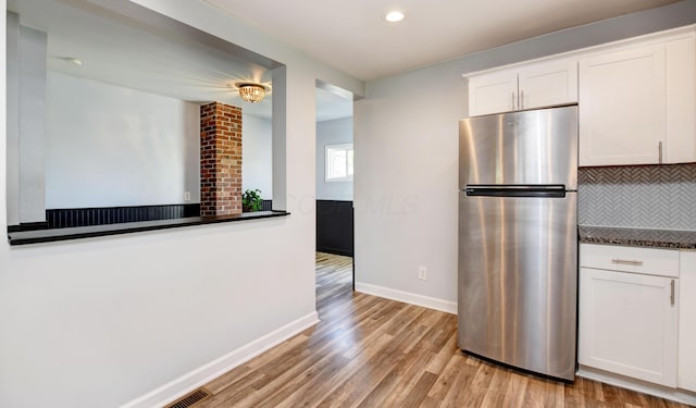 kitchen with decorative backsplash, light wood-type flooring, baseboards, white cabinets, and freestanding refrigerator