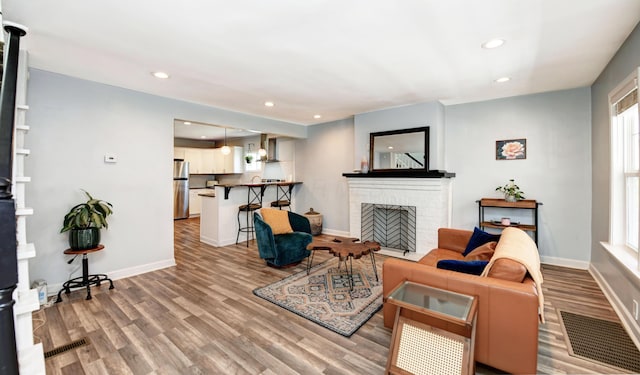 living room featuring a brick fireplace, baseboards, visible vents, and wood finished floors