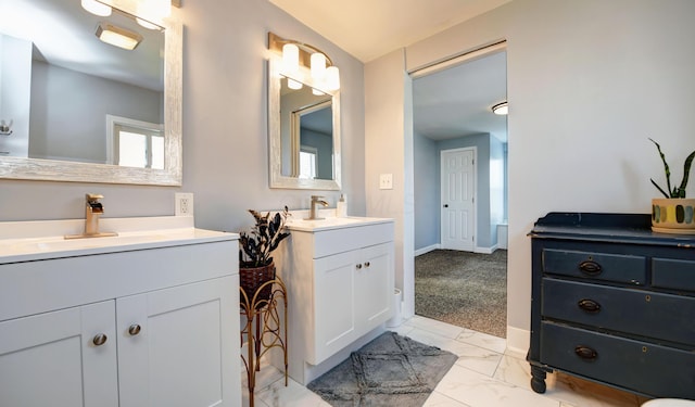 full bath with baseboards, two vanities, a sink, and marble finish floor