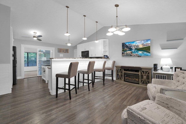 kitchen with a breakfast bar area, black microwave, dark wood finished floors, white cabinets, and lofted ceiling