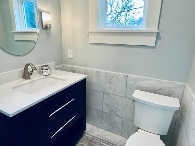 half bathroom with toilet, tile walls, wainscoting, and vanity