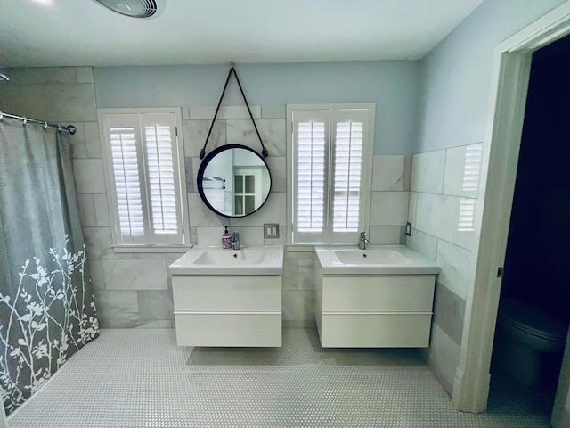 bathroom featuring tile walls, a sink, two vanities, and a healthy amount of sunlight