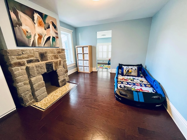 bedroom with baseboards, a stone fireplace, and wood finished floors