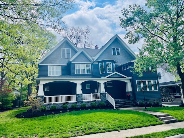 view of front of home with a front lawn, stone siding, covered porch, and a chimney