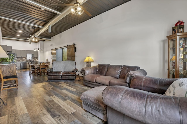 living room with dark wood finished floors, a barn door, beamed ceiling, and ceiling fan