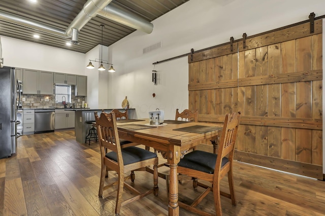 dining space with a high ceiling, visible vents, a barn door, and dark wood finished floors