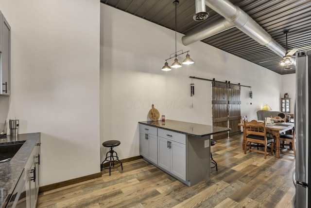 kitchen featuring hanging light fixtures, a breakfast bar, a barn door, dark wood-style floors, and a peninsula