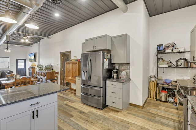 kitchen with dark stone countertops, gray cabinets, stainless steel appliances, light wood-style floors, and backsplash