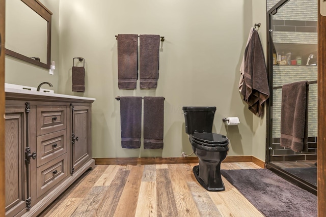 bathroom with toilet, vanity, wood finished floors, and baseboards