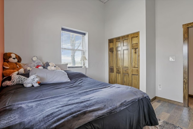 bedroom with baseboards, wood finished floors, a closet, and a towering ceiling