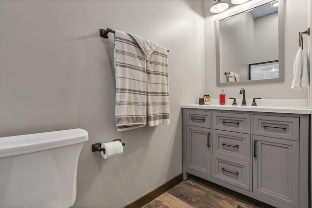 half bathroom featuring baseboards, wood finished floors, toilet, and vanity