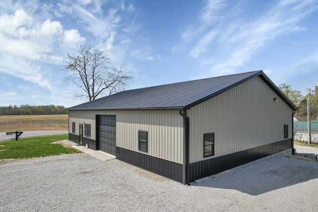 view of side of property featuring a garage, an outdoor structure, driveway, and metal roof