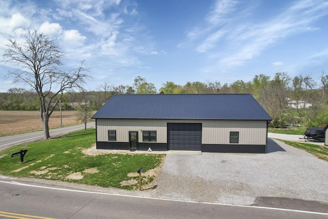 view of front facade with an outdoor structure, gravel driveway, metal roof, a detached garage, and a front yard