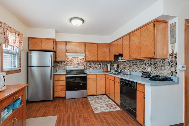 kitchen with under cabinet range hood, wood finished floors, appliances with stainless steel finishes, and light countertops