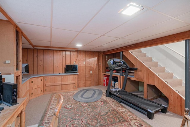 exercise room featuring wooden walls, carpet floors, and a drop ceiling
